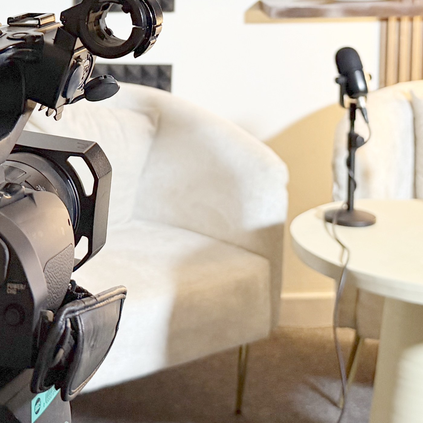 Detail of the Kontext Media studio: a microphone on a stand beside an interview chair, with a broadcast camera in the foreground